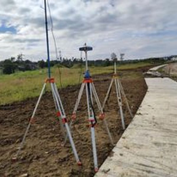 Three surveying tripods set up near a newly paved pathway.