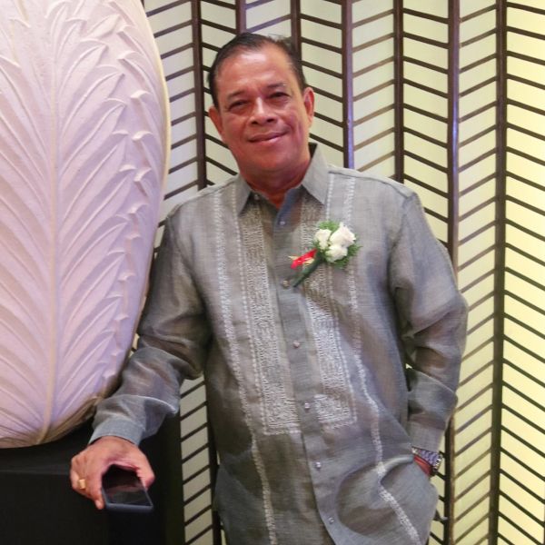 Man in traditional embroidered shirt posing with a flower corsage.