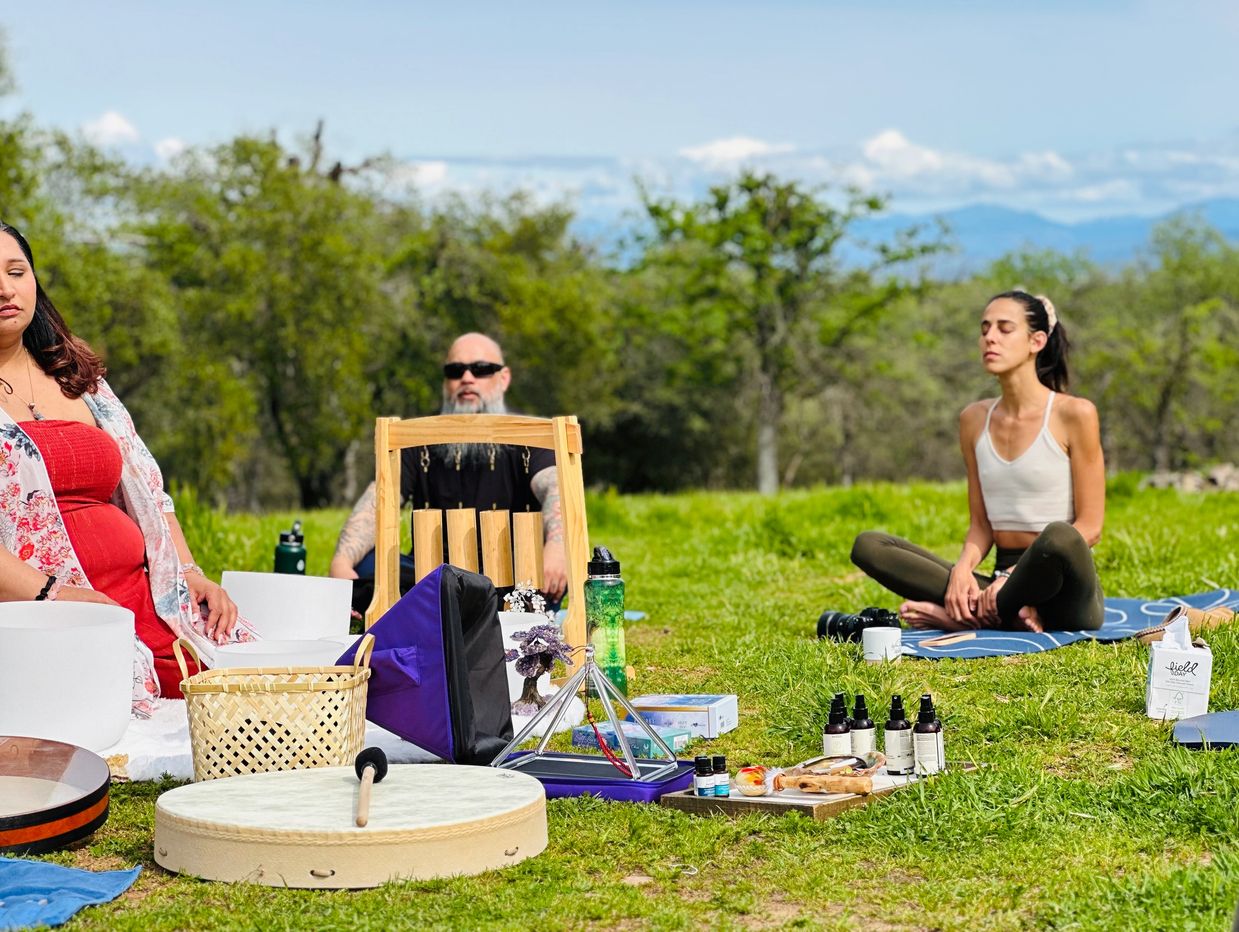 Three people meditating outdoors with spiritual tools.