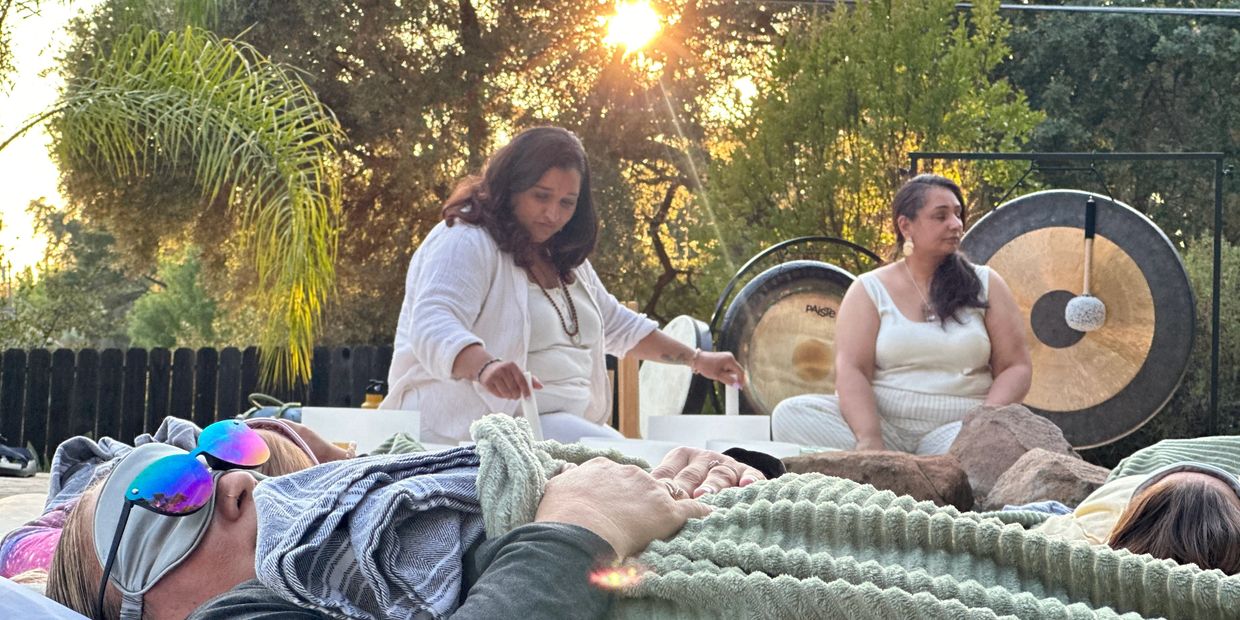 Group meditation or healing session outdoors with gongs at sunset.