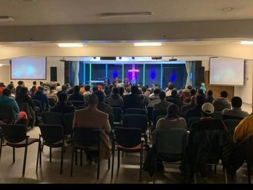 Congregation gathered in a church with a lit cross at the front.