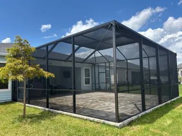 A large screened patio enclosure attached to a house under a blue sky.