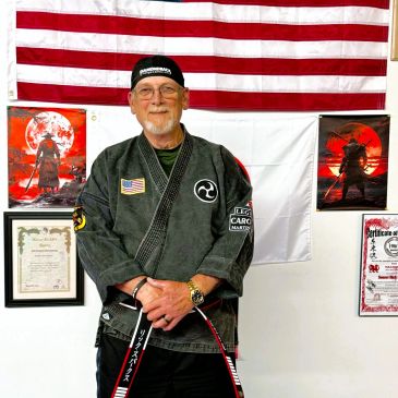 Elderly man in martial arts attire with flags and certificates.