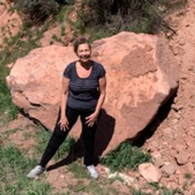 Person standing outdoors near a large rock and greenery.