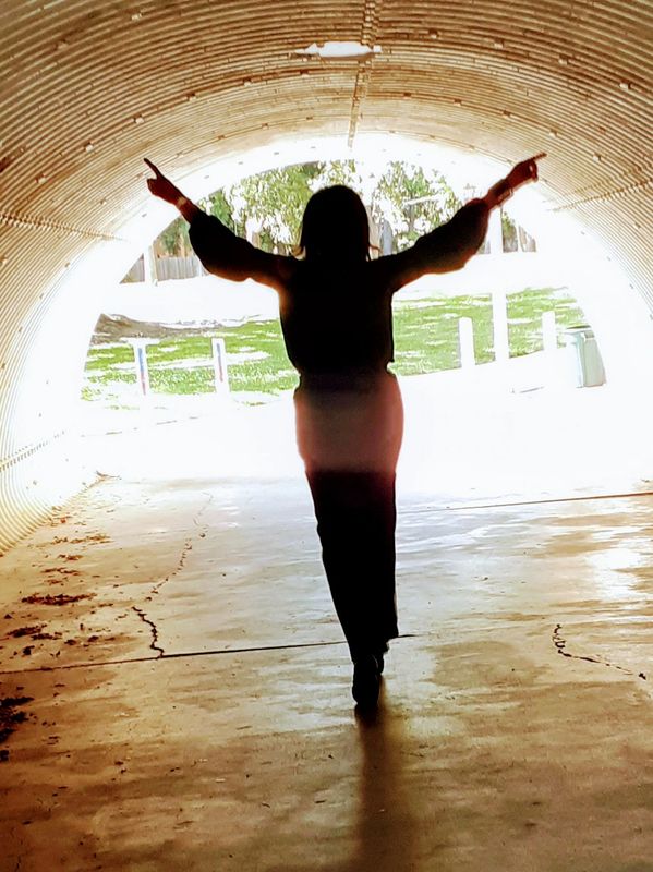 Silhouette of person with arms raised inside a bright tunnel.