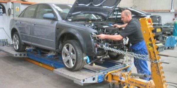 Mechanic repairs car front using a frame straightening machine.