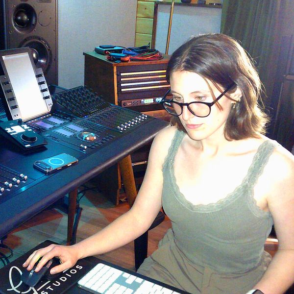 Young woman working at an audio mixing console in a studio.
