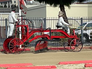 Two men dressed in white operating a vintage red road grader.
