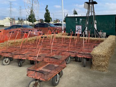 Orange metal carts lined up outdoors near hay bales under a clear sky.