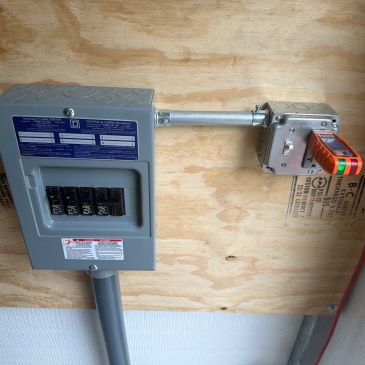 Electrical breaker panel with safety switch installed on plywood wall.