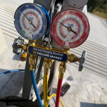 Close-up of Yellow Jacket test and charging manifold gauges with blue, yellow, and red hoses.