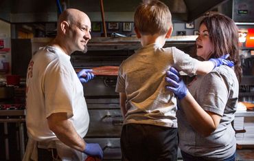 Parents helping son cook a pizza in a commercial oven.  Branding cat house pizza photo session