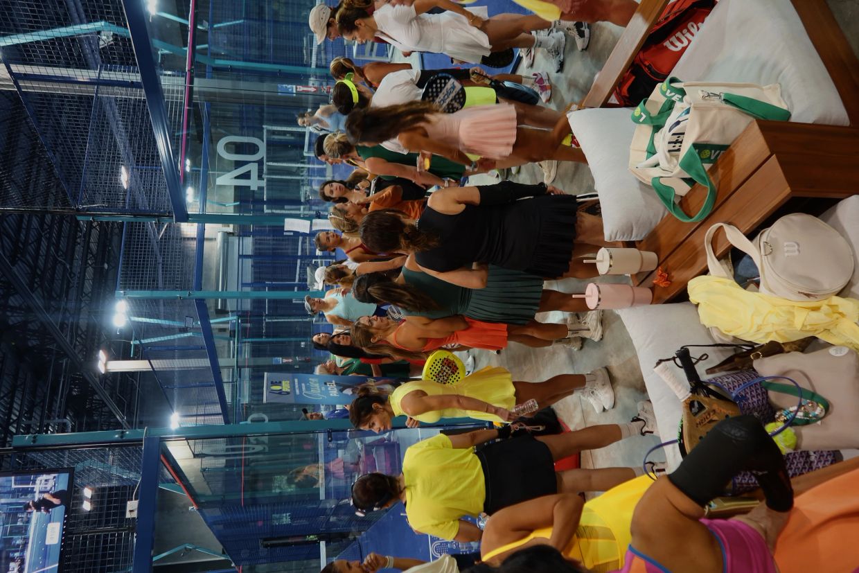Women gathered at a paddle tennis court, many wearing colorful sports dresses.