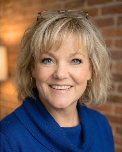 Image of Amy Grove smiling in a blue shirt with a brick wall background.