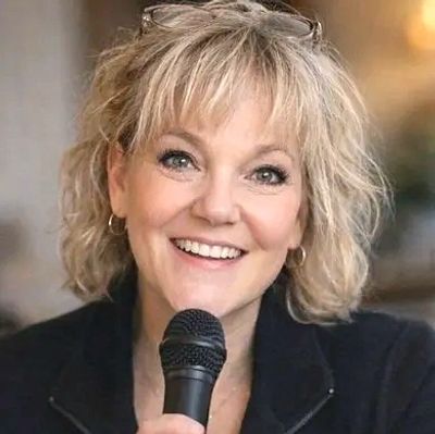 Picture of Amy Grove smiling and holding a microphone while speaking.