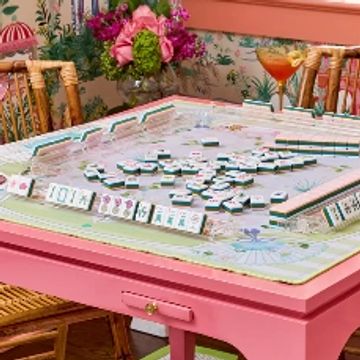 A colorful mahjong game set on a pink table with drinks and flowers.