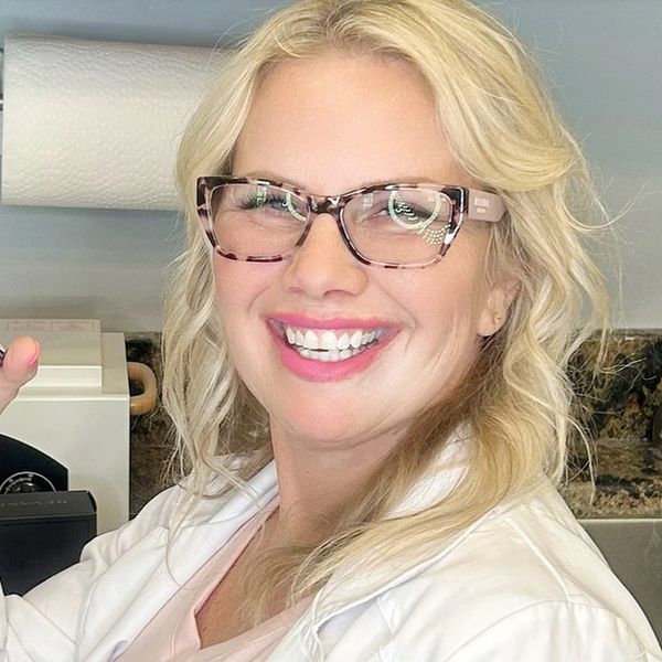 Smiling woman with blonde hair and glasses in a white coat.