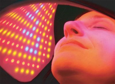 Woman undergoing LED light therapy with colorful lights on her face.