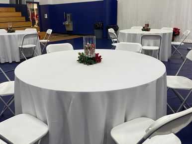 Round table with white tablecloth and centerpiece in a gymnasium setting.