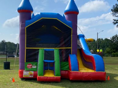 Inflatable bounce house with slide set up on a grassy field under a blue sky.