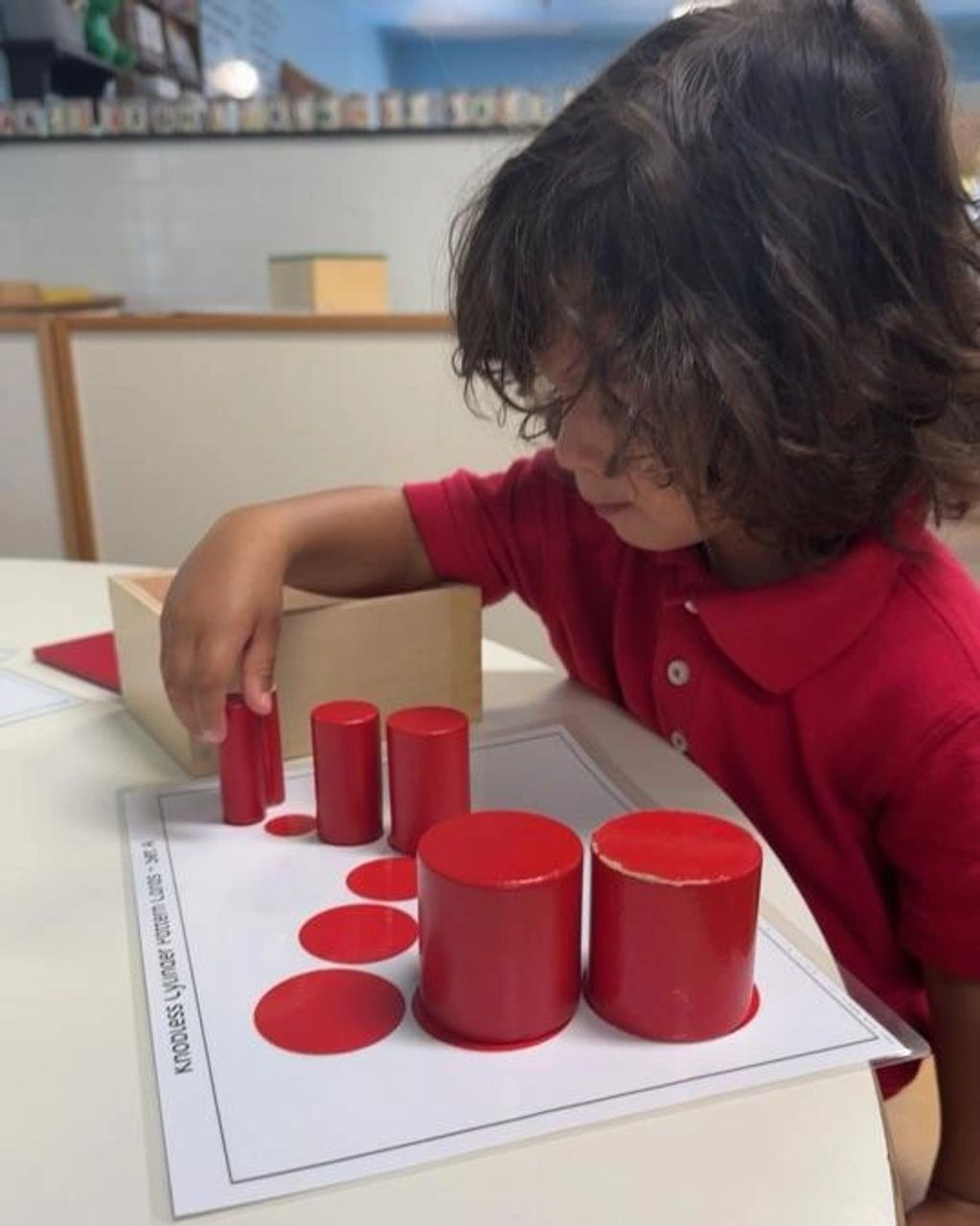 Child matching red cylinders to their corresponding flat circles in a learning activity.