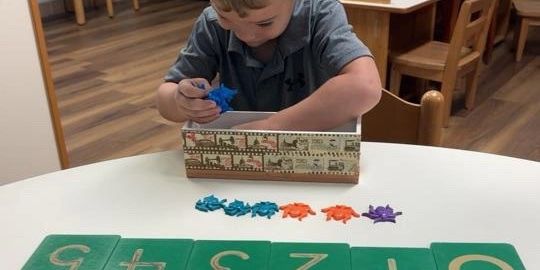 A young boy playing with colorful star-shaped toys and number cards in a classroom.