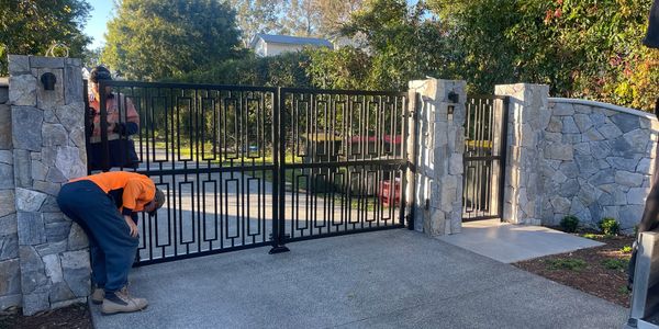 A person in an orange shirt inspecting a modern black metal gate at a stone entrance.