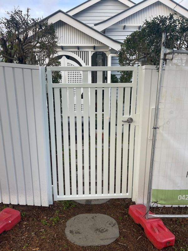 A white picket gate leading to a house with a circular stepping stone in front.