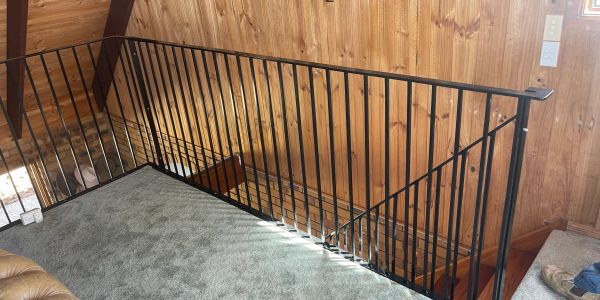 Black metal railing on a carpeted loft with wooden walls.