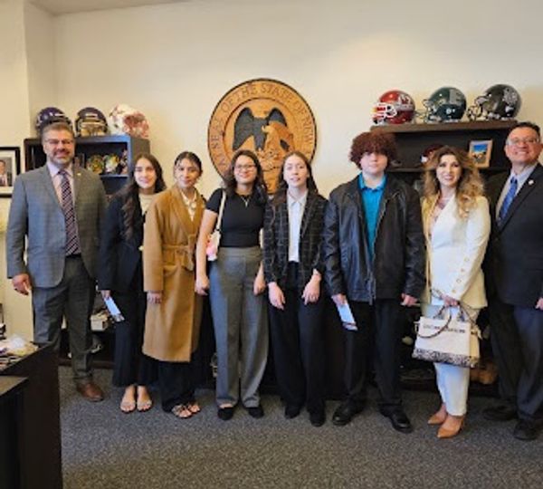 Group photo of eight people standing indoors near state seal.