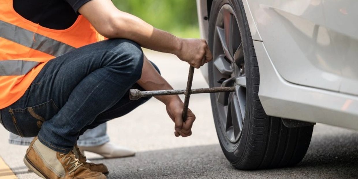 A person in an orange vest changing a car tire on the road.