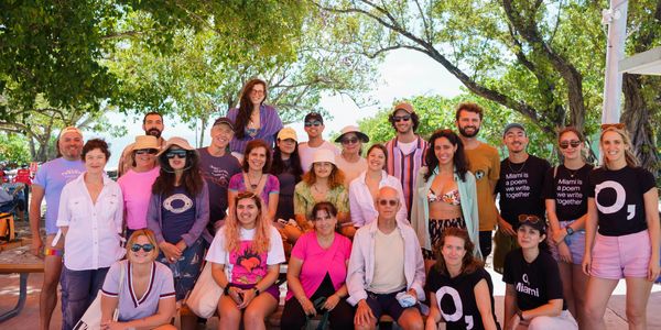 A diverse group of people posing together outdoors under trees.