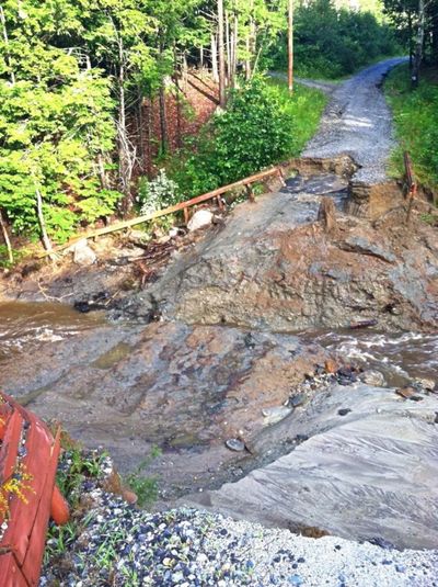 A dirt road washed out by heavy water flow, blocking passage.