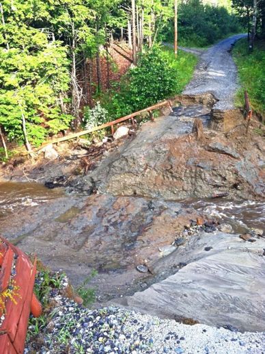 A washed-out gravel road with broken railings and muddy debris.