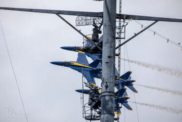 Blue Angels jets flying in close formation behind a tower.