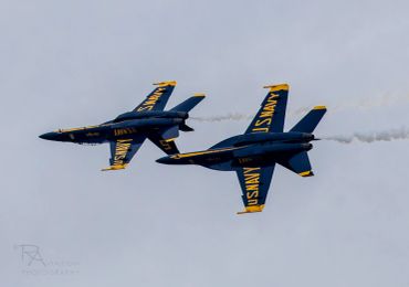 Two U.S. Navy Blue Angels jets perform a close aerial maneuver.