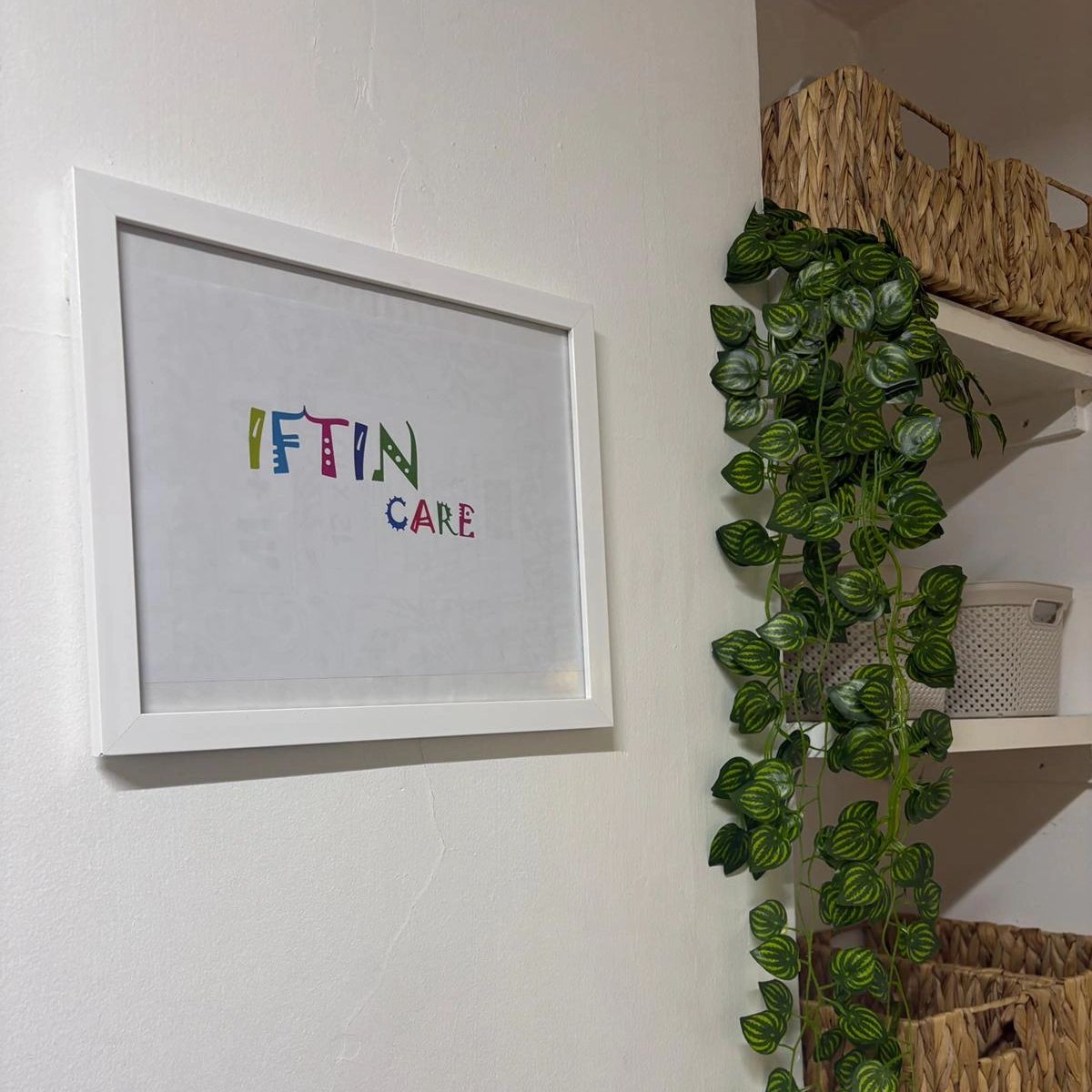 Framed colorful text artwork on wall with hanging plant and wicker baskets.
