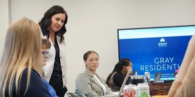 A group of professionals in a meeting room discussing work with laptops and a presentation screen.