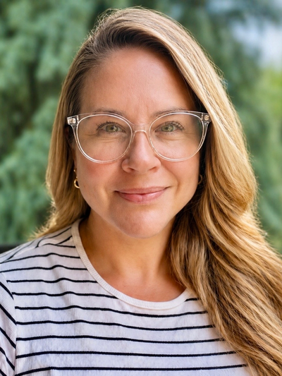 Smiling woman with clear glasses and striped shirt outdoors.