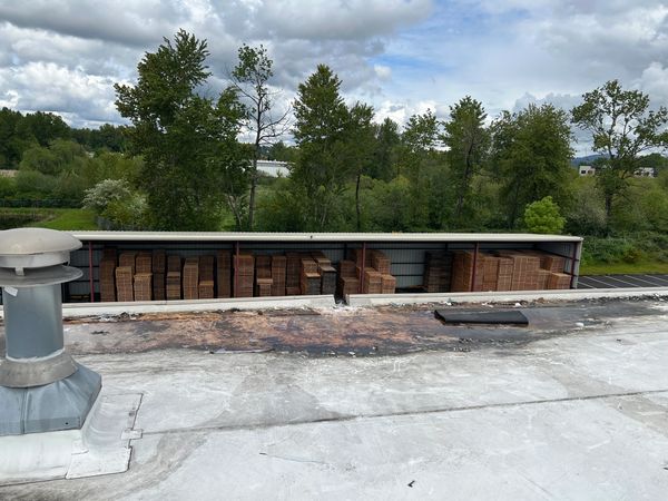 Stacks of wooden pallets stored under a metal shelter near trees and cloudy sky.