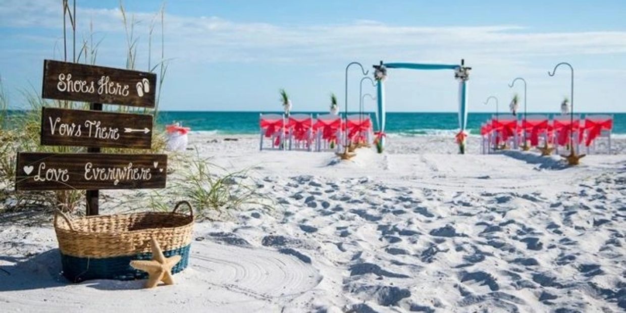 Beach wedding setup with signs, chairs, and an arch by the ocean.