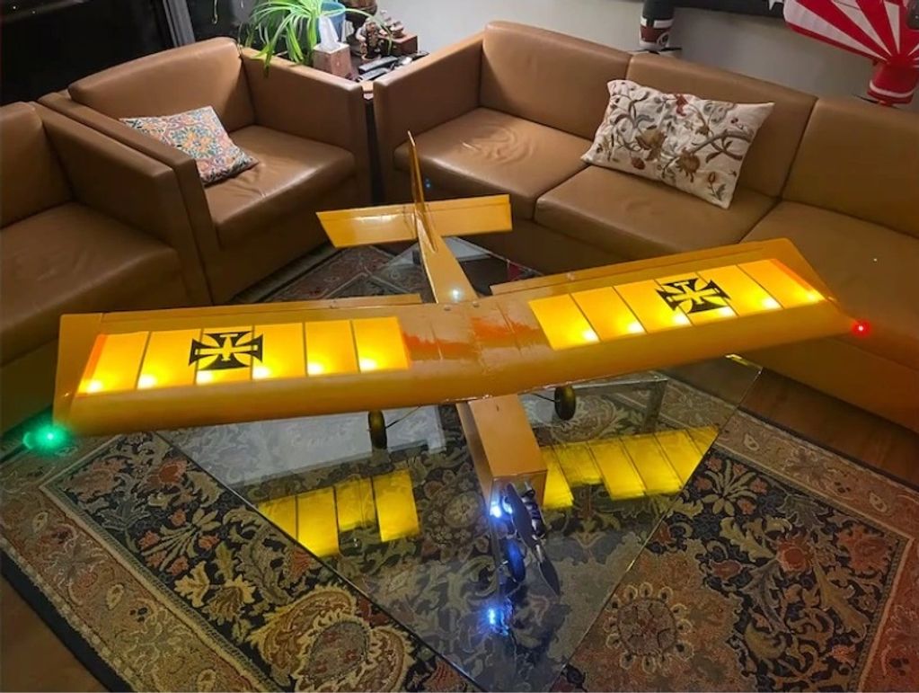 Yellow model airplane with lit wings on a glass table in a living room.