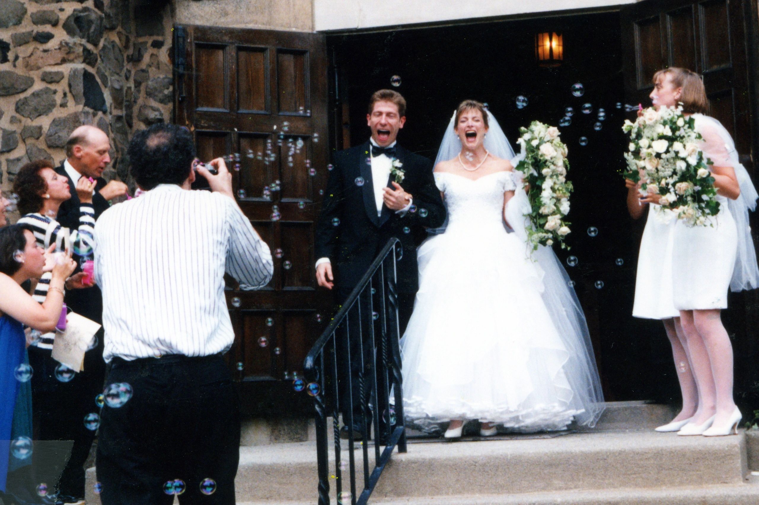 Bride and groom laugh as guests blow bubbles at their wedding exit.