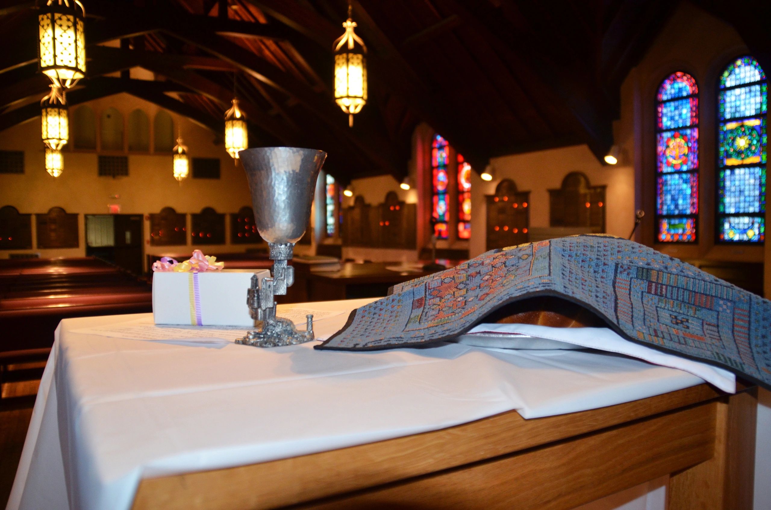 Communion cup and folded prayer cloth on altar in a church with stained glass windows.