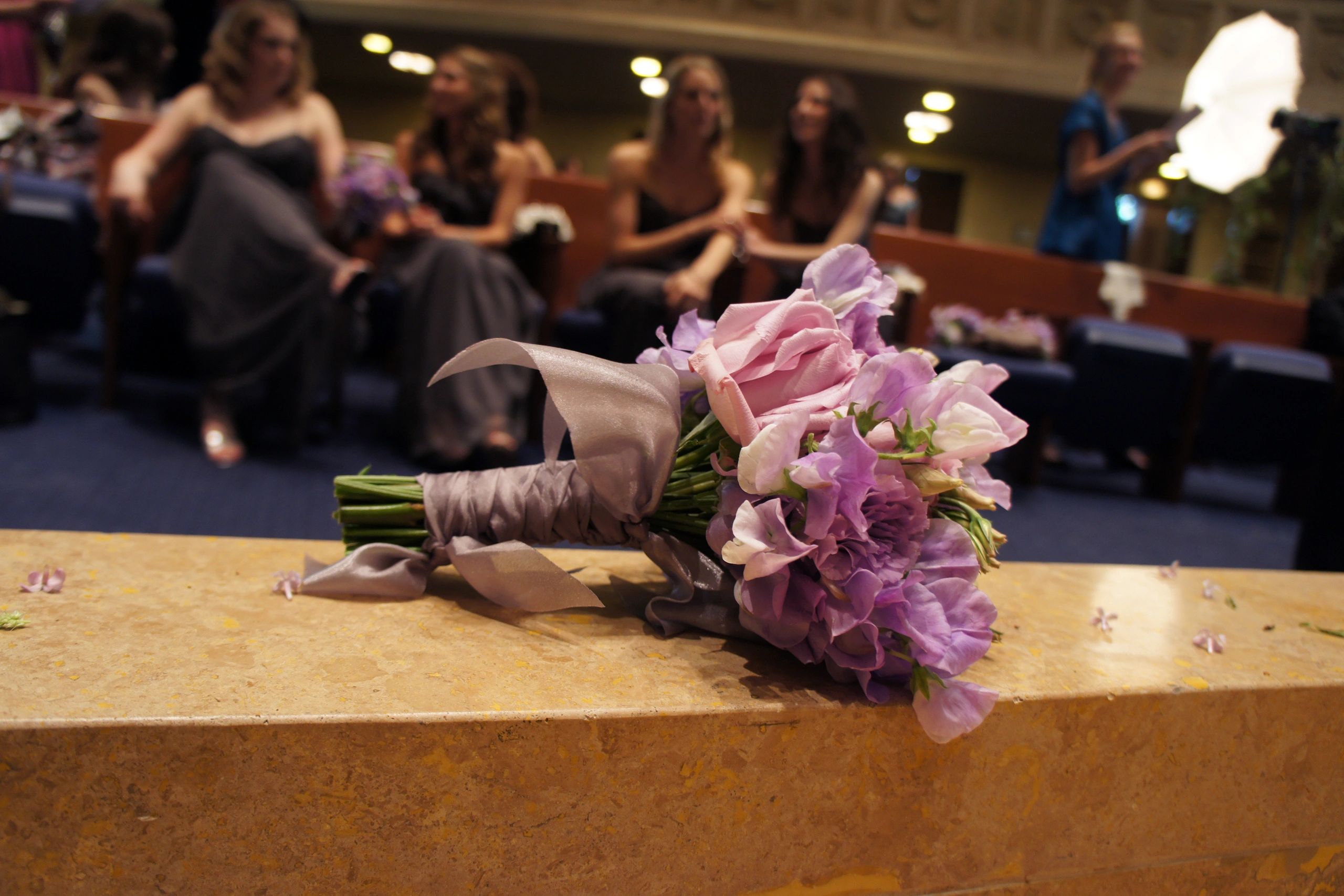 A delicate purple and pink bridal bouquet rests on a stone ledge.