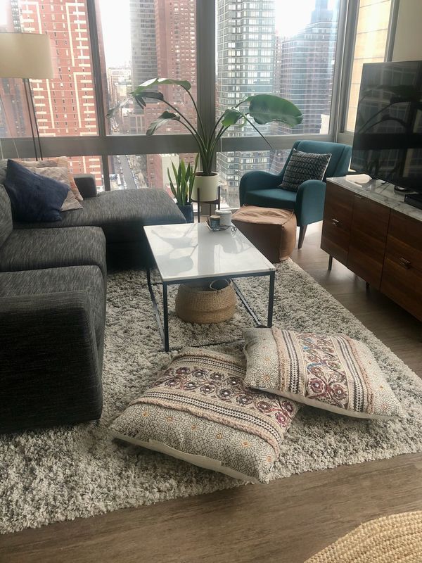 Cozy living room with large windows, a gray sofa, a blue armchair, and patterned floor cushions.