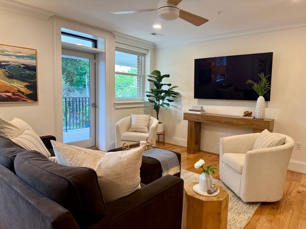 Cozy living room with neutral tones, modern furniture, and natural light from a balcony door.