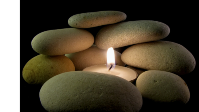 Stacked smooth stones around a lit candle.