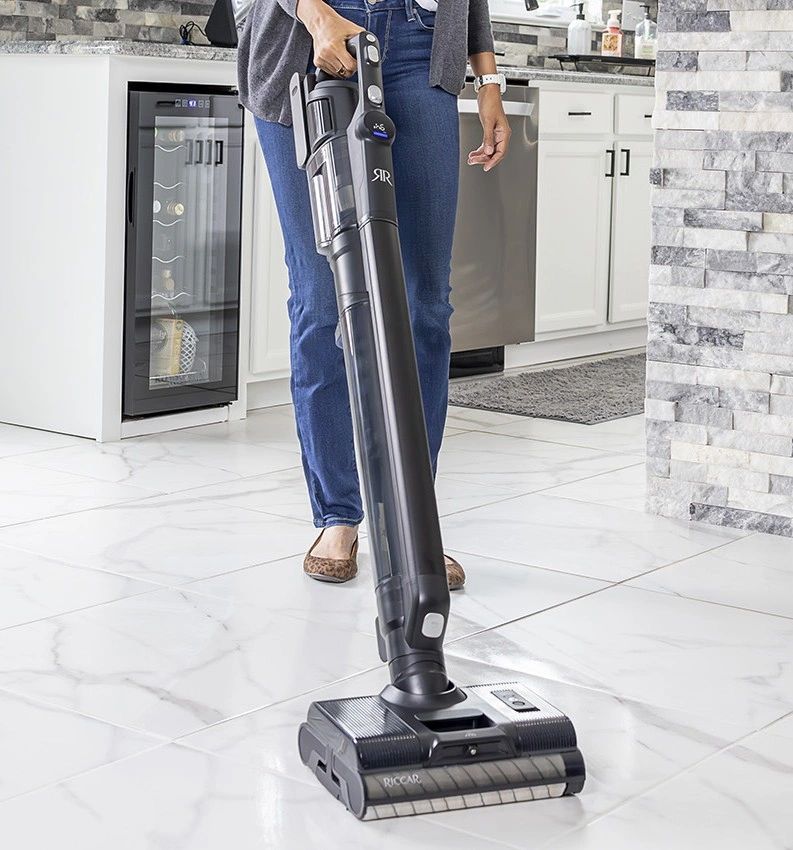 Person vacuuming a clean, modern kitchen floor with a sleek Riccar vacuum.