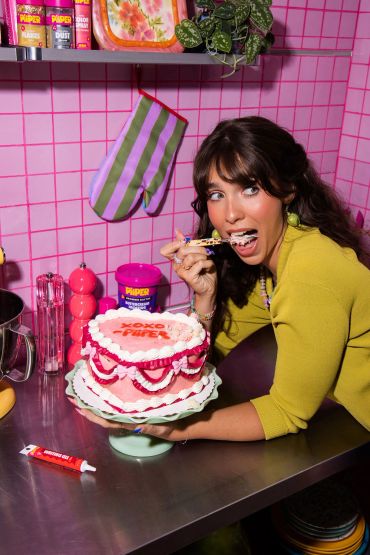 Woman eating cake in vibrant pink kitchen.